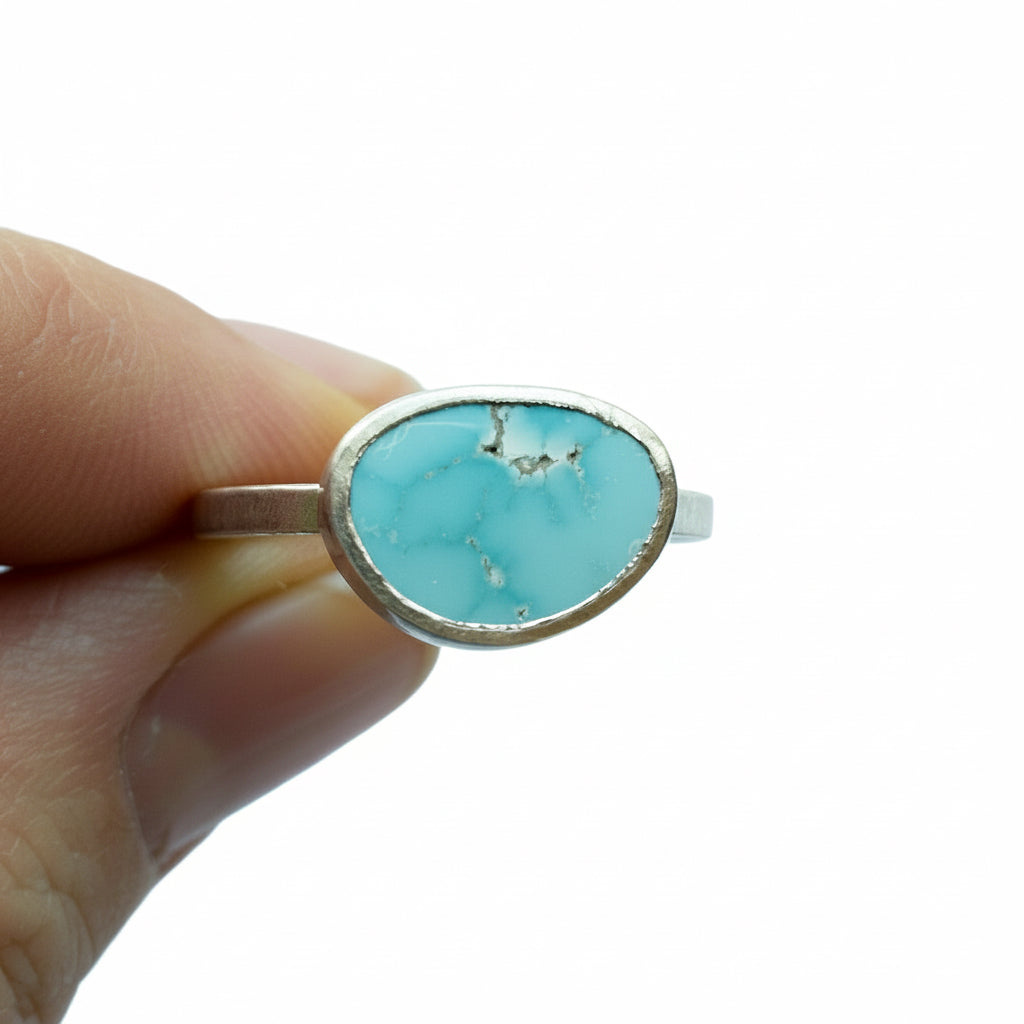 Turquoise ring with silver band held by a hand on a white background