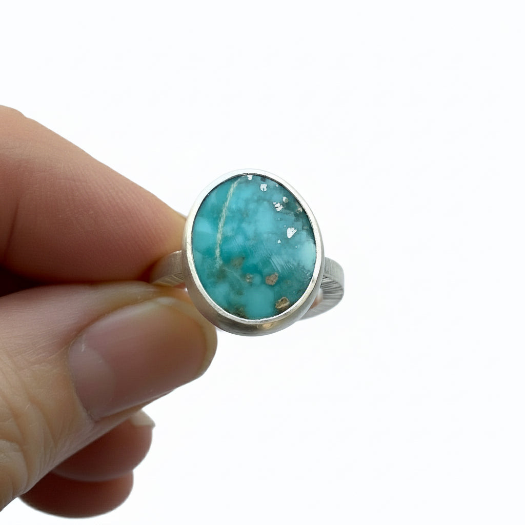 Turquoise ring held in a hand against a white background