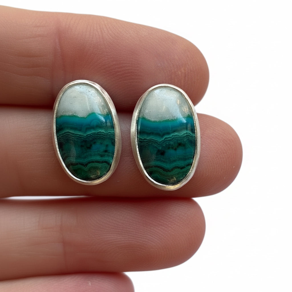 Pair of earrings with green and white stone held between fingers against a light background