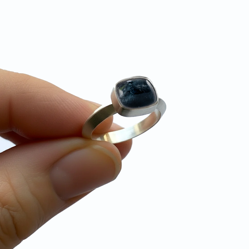 Silver ring with a blue tourmaline gemstone held in a hand against a light background