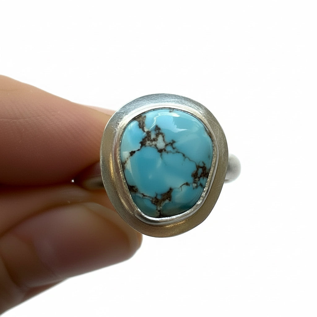 Turquoise stone ring held by a hand on a white background