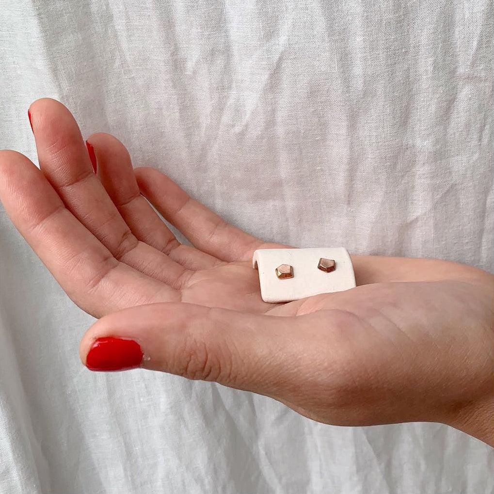 Hand holding a small white box with gold earrings against a light fabric background