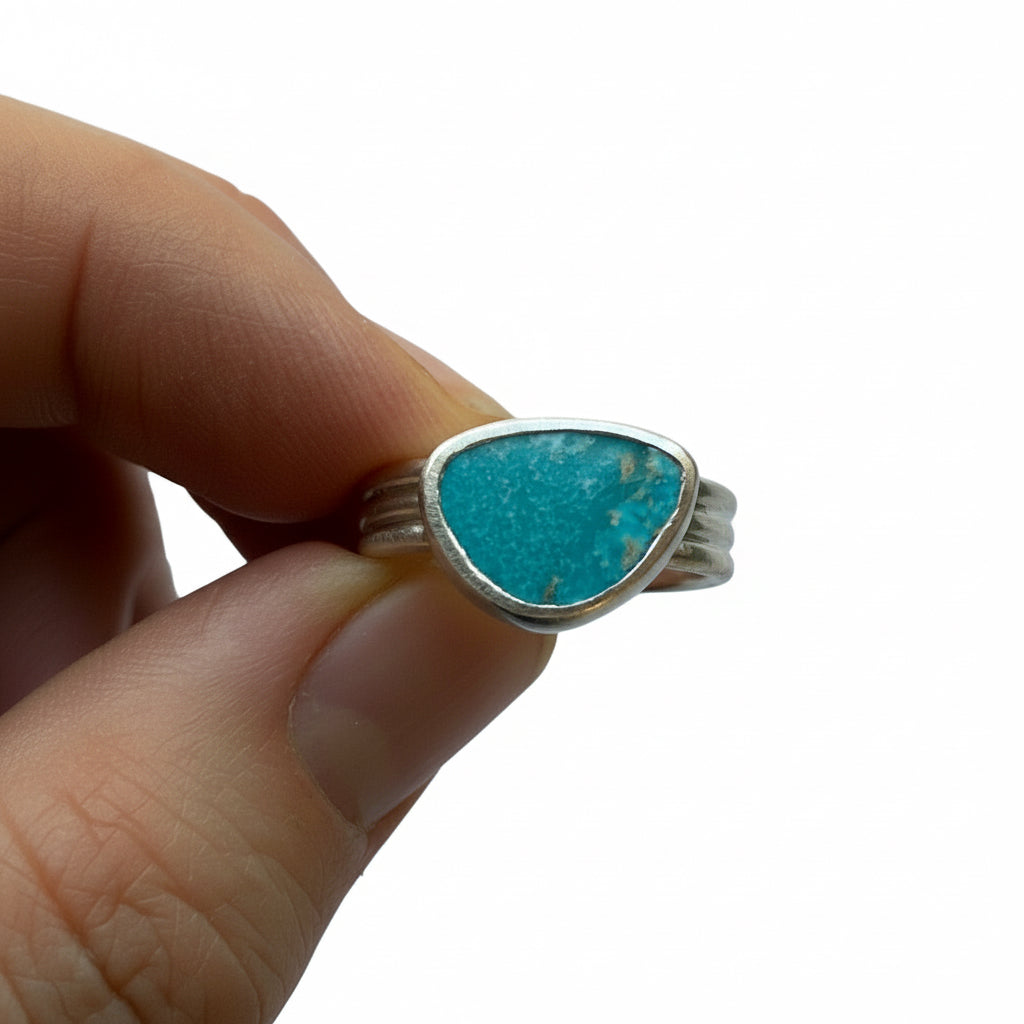 Turquoise ring with silver band held by a hand against a plain background