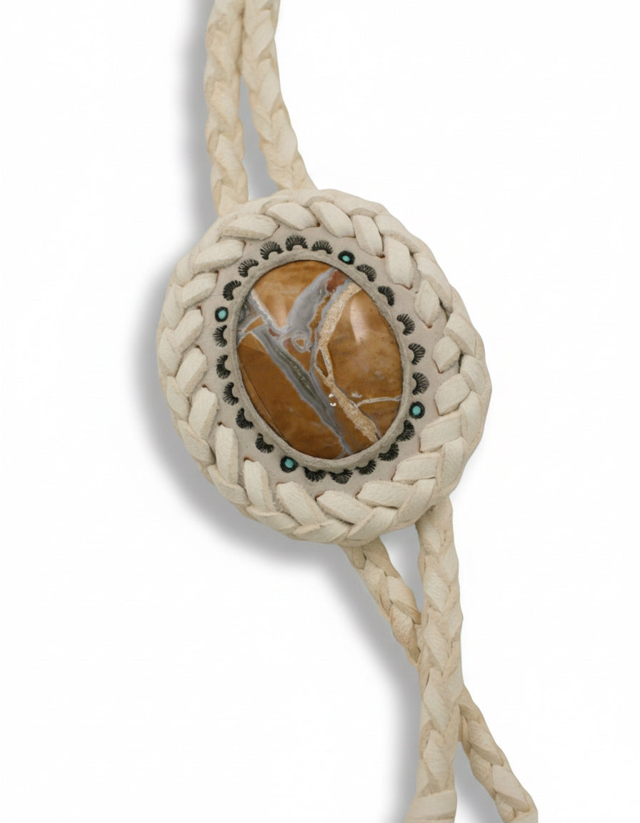 Close-up of hand-tooled white leather bolo tie featuring a Willow Creek jasper stone centerpiece by Kelly Horrigan Handmade, shown on white background.