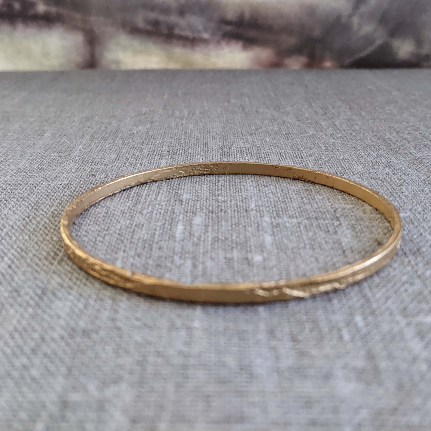 Single thin etched bangle in 22k gold-plated brass shown on a textured grey surface.