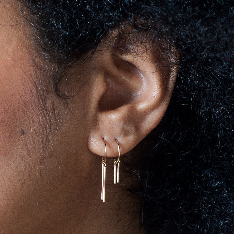 Baby Chime 14k gold earring worn on ear – close-up showing delicate minimalist dangle design.