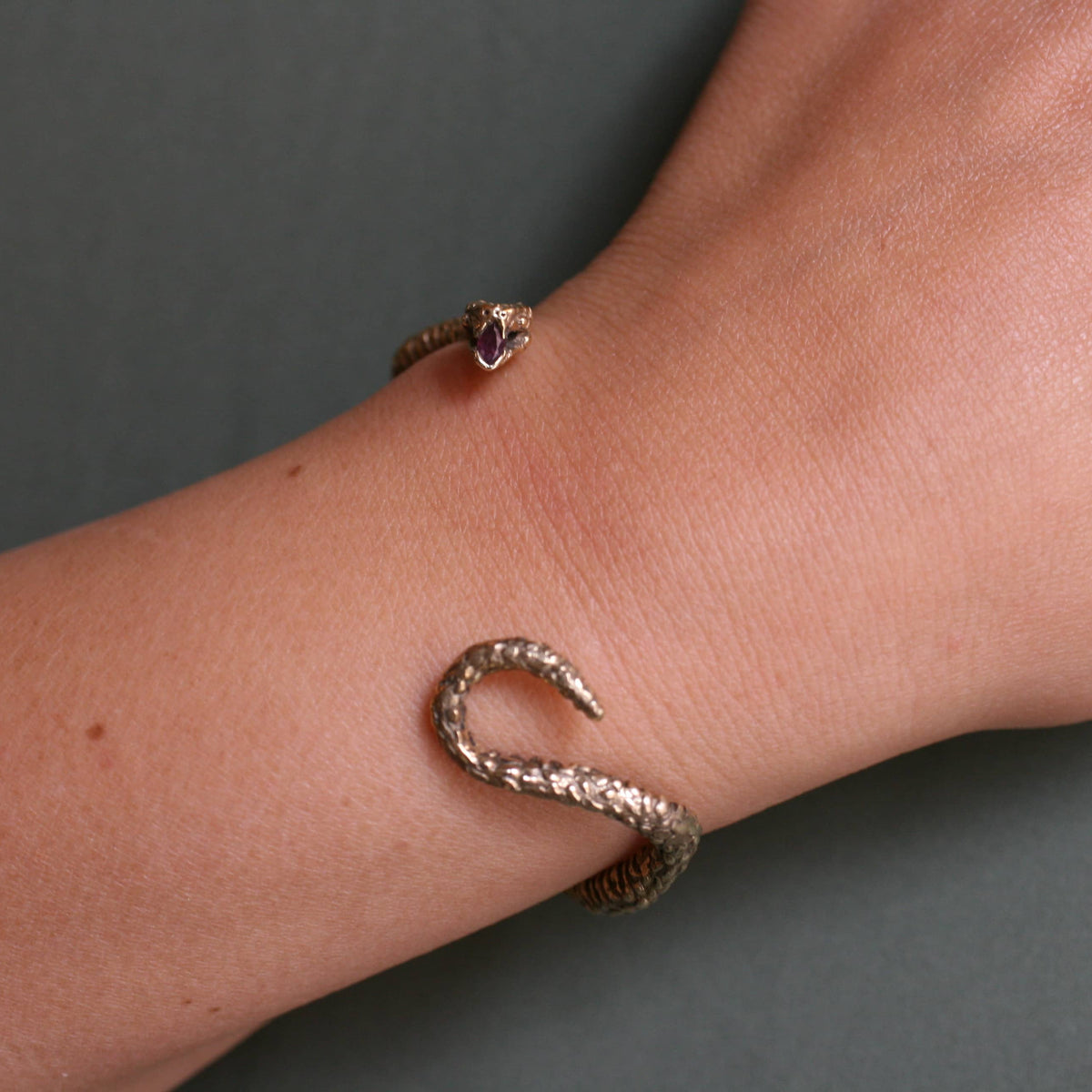 Close-up of the sterling silver Ichos Snake Cuff worn on the wrist, highlighting its textured snake body and sculptural gemstone-set head.