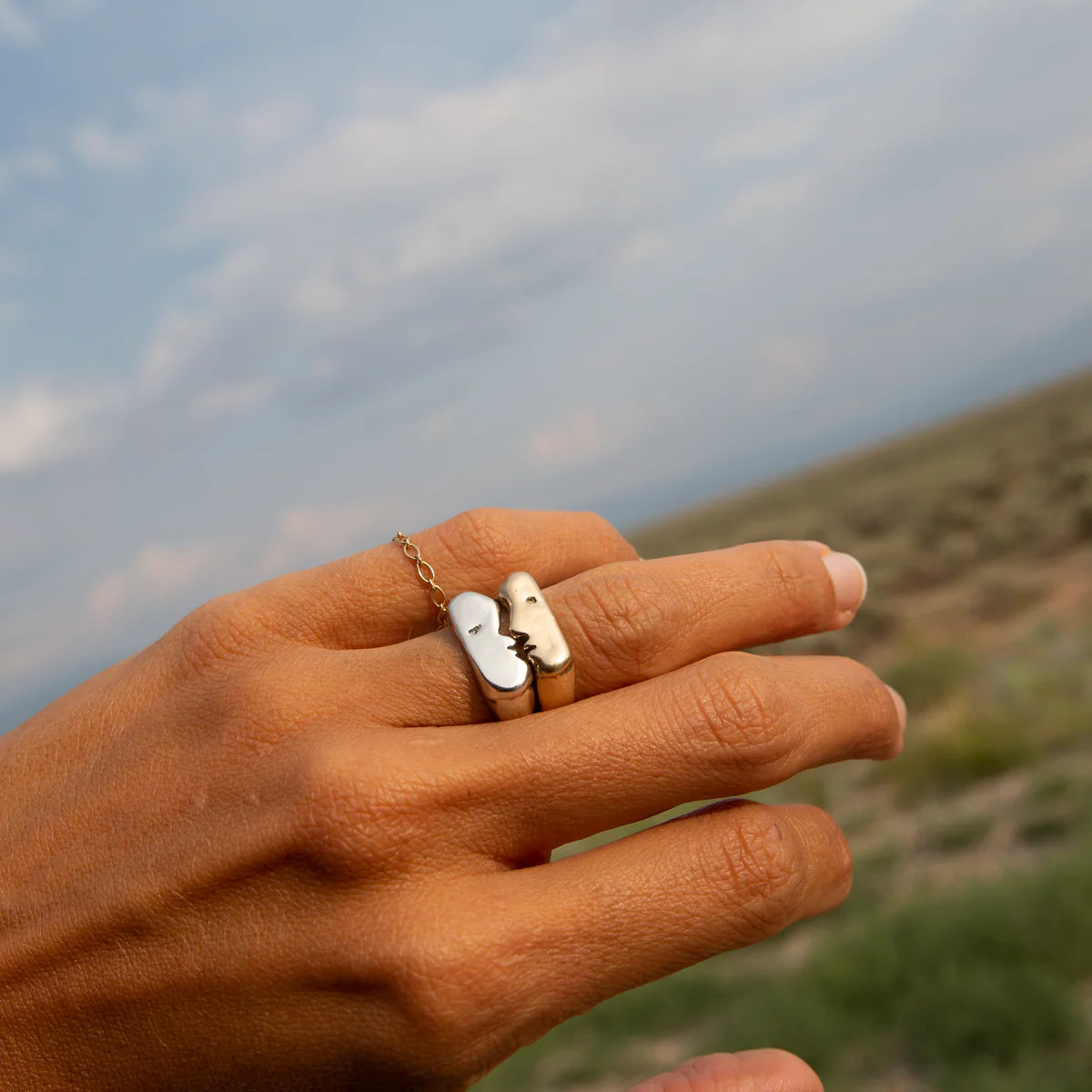 Model wearing kissing signet rings outdoors, showing how the silver and gold pair interlocks on the hand.
