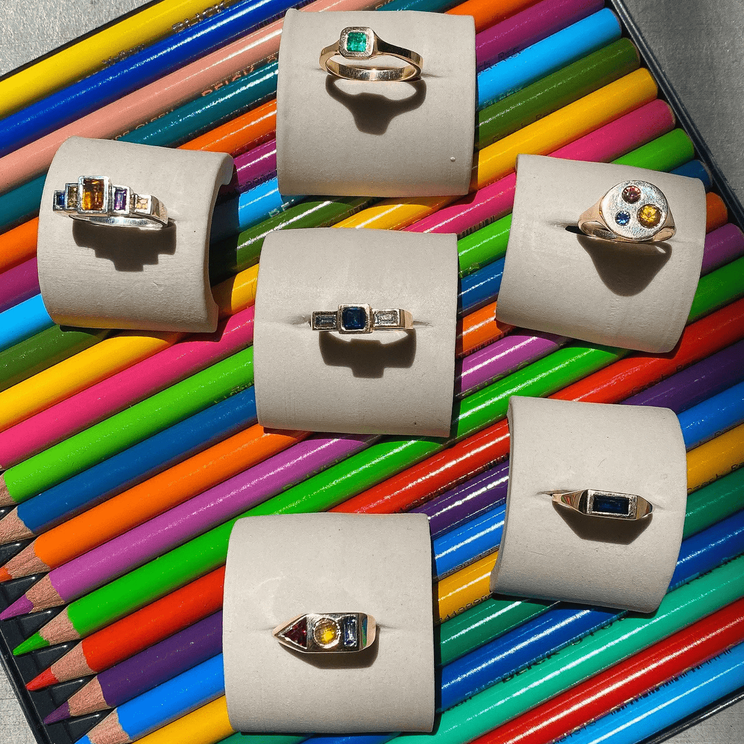 Styled display of multiple Adeline Jewelry signet rings arranged on colorful pencils.