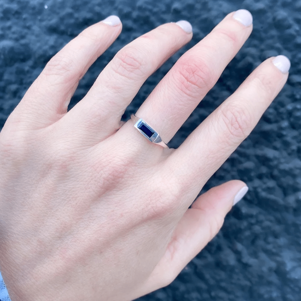 Sterling silver signet ring with sapphire baguette worn on a hand outdoors.