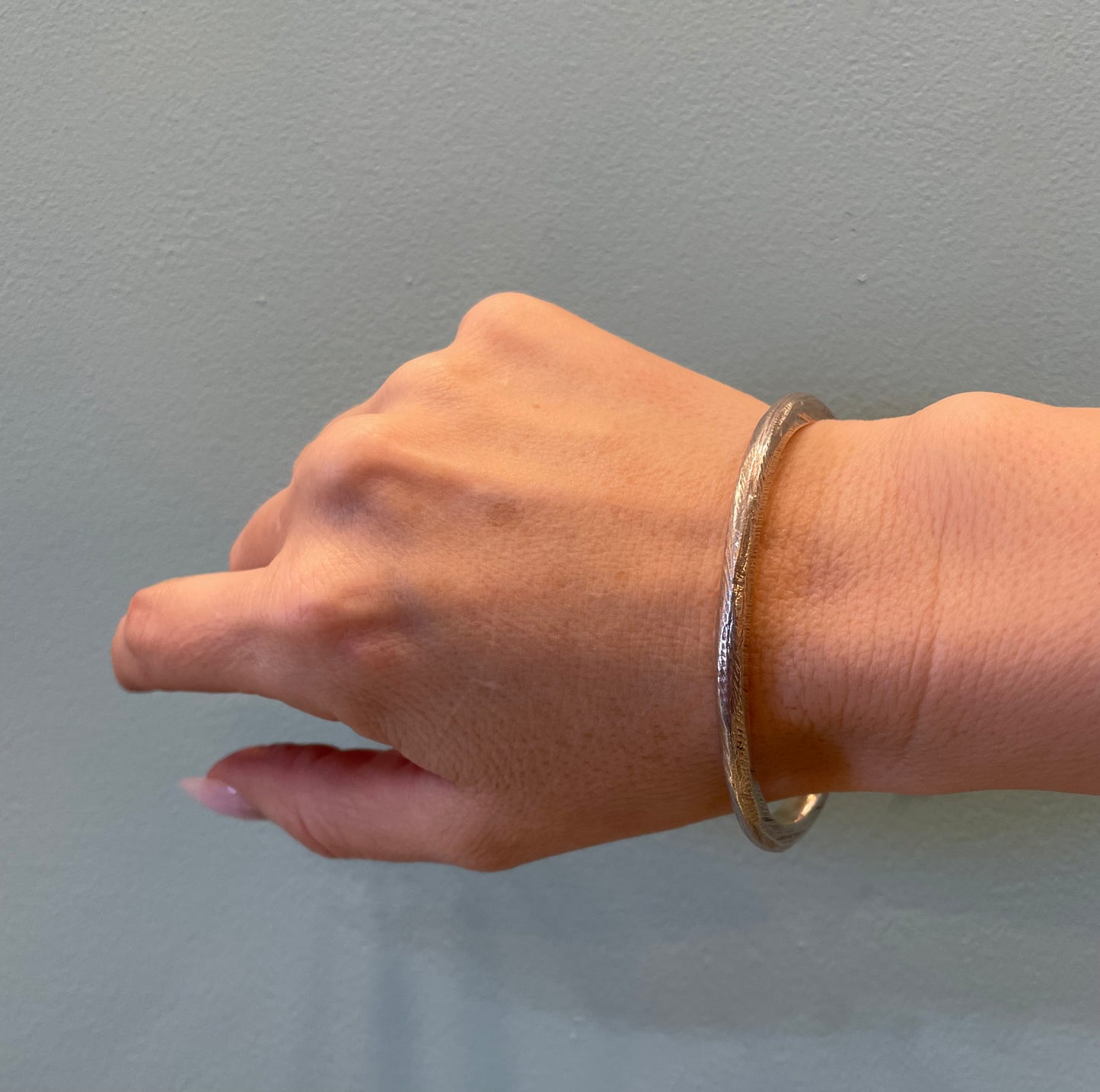 Model wearing the sterling silver Reyes Textured Bangle Bracelet by Ladha Jewelry, showing its delicate proportions and fit on the wrist.