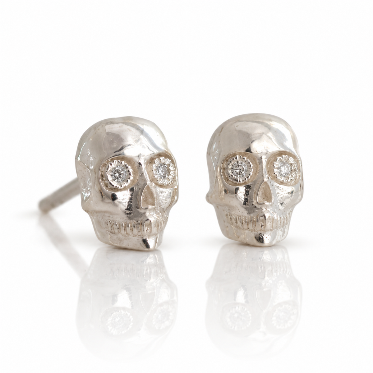 Angled view of handcrafted sterling silver skull stud earrings by Michaela Farkasovska, highlighting their dimensional skull details and diamond accents.
