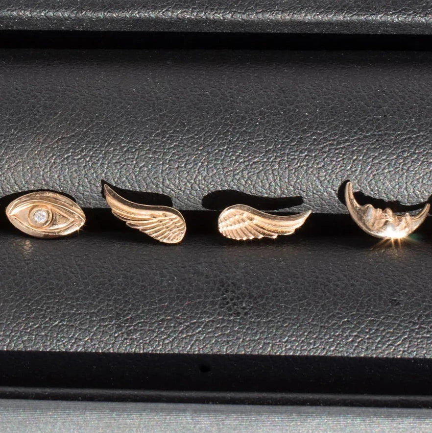 Handcrafted 14k yellow gold Wing Stud Earrings displayed alongside other gold jewelry, highlighting their delicate sculptural design.