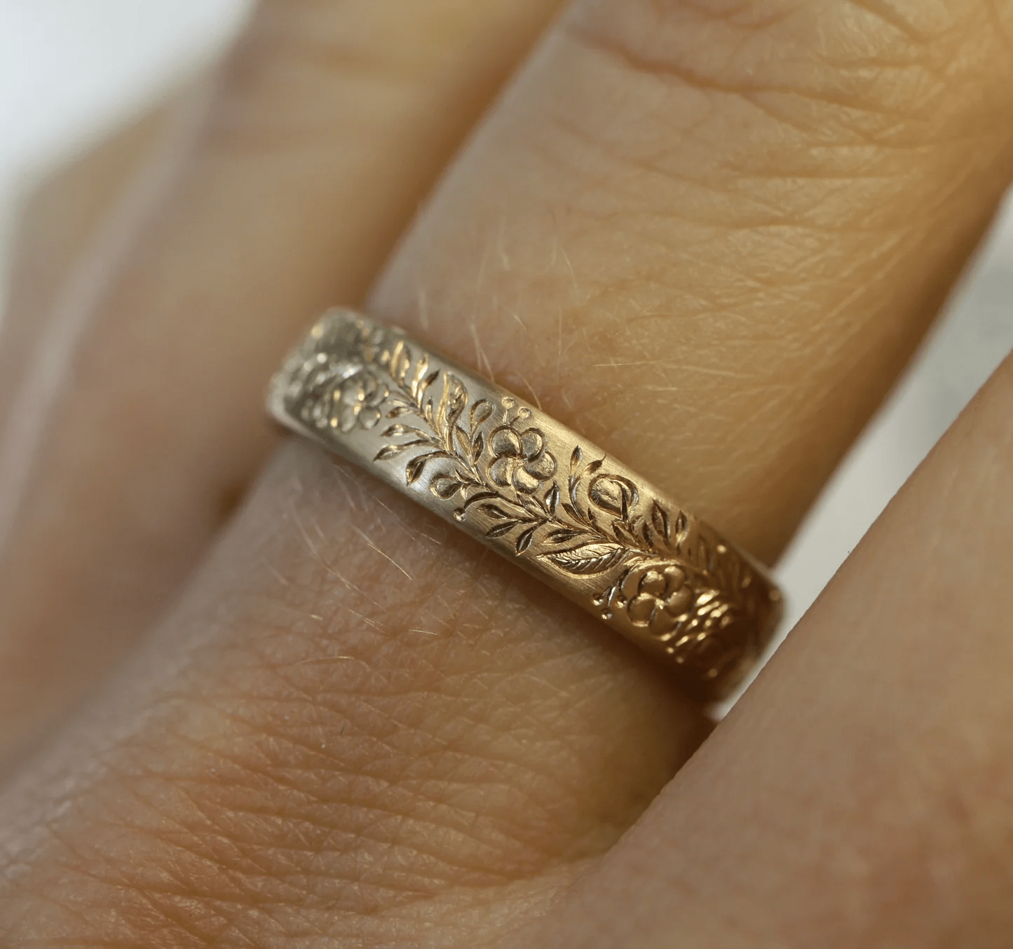 14k gold engraved floral band ring worn on a finger, showing detailed hand engraving.