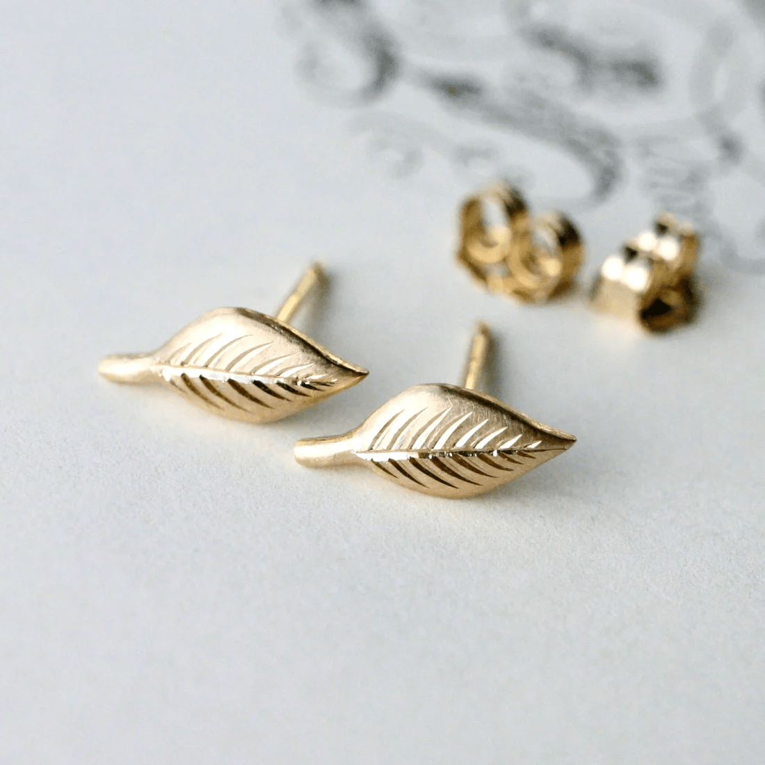 14k gold hand-engraved leaf stud earrings displayed on a light background.