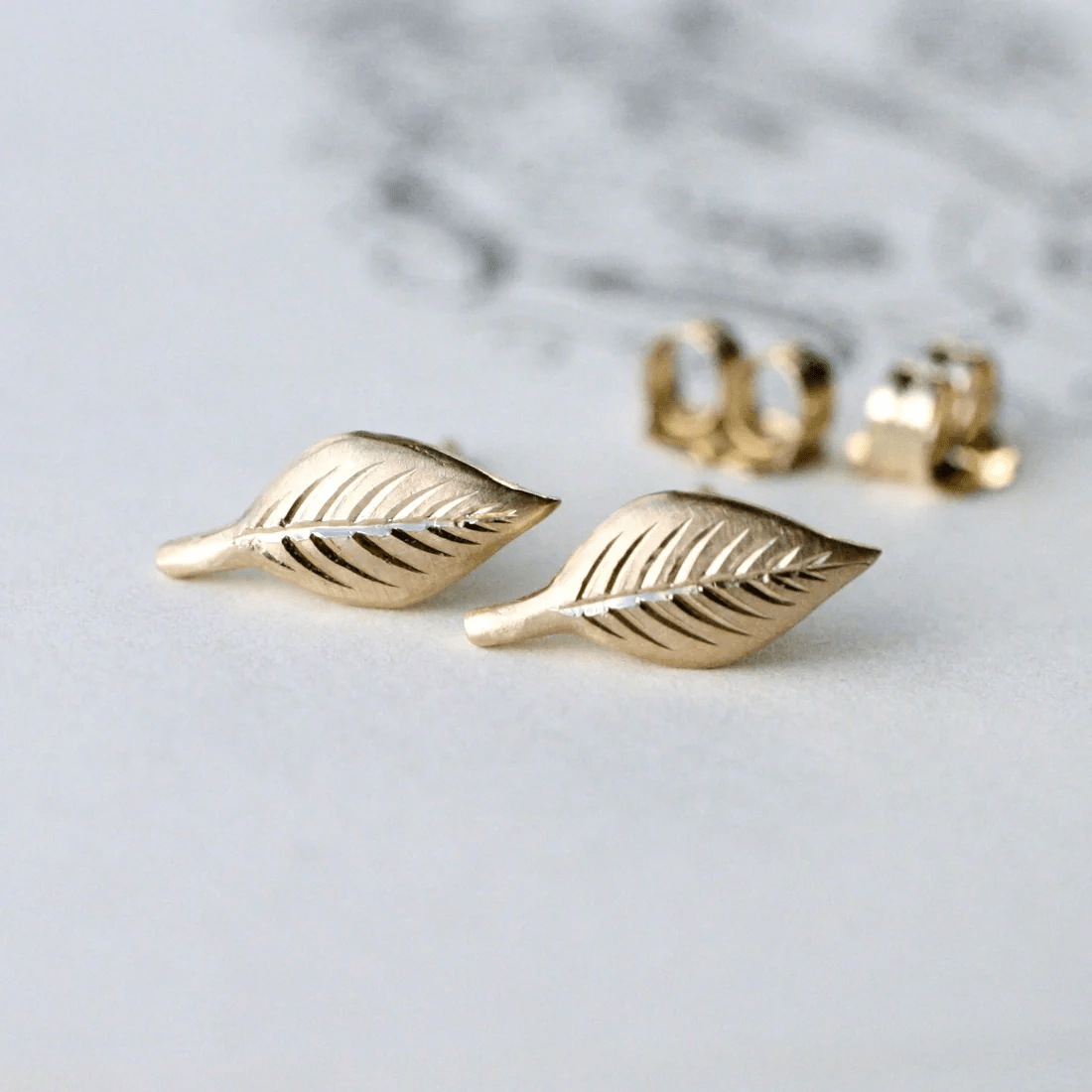 Close-up of 14k gold engraved leaf stud earrings with detailed hand engraving.