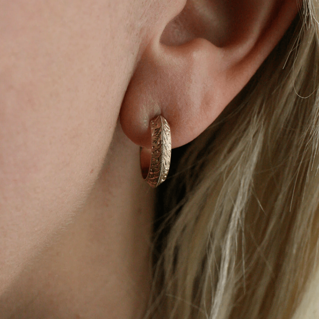 Side view showing the detailed floral engraving on 14k gold hoop earrings, worn on the ear.