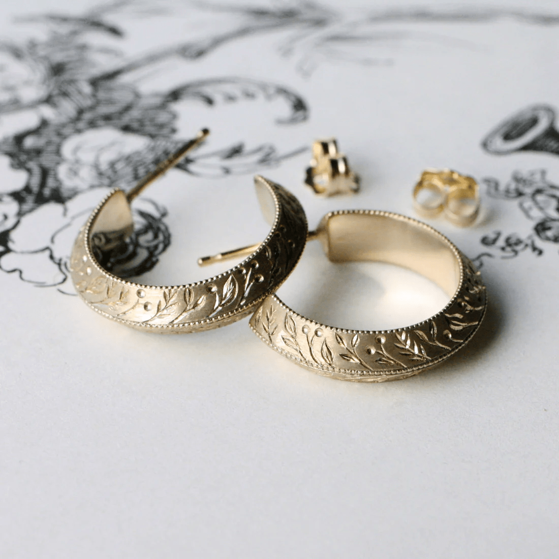 Hand-engraved floral pattern on 14k gold hoop earrings displayed with earring backs.