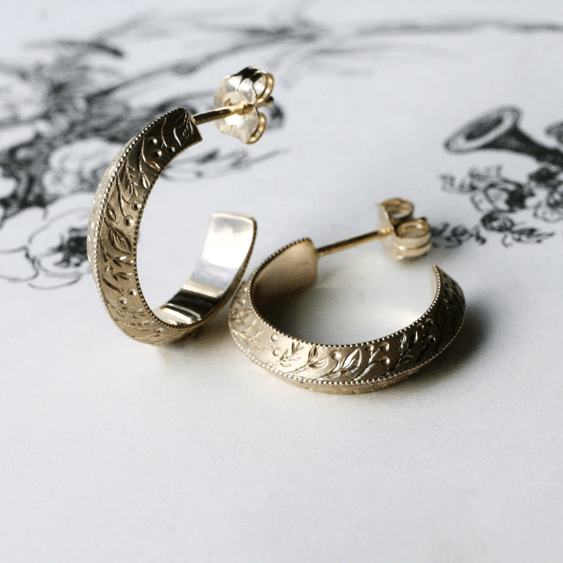 Handmade 14k gold floral hoop earrings showing engraved detail and polished inner surface.