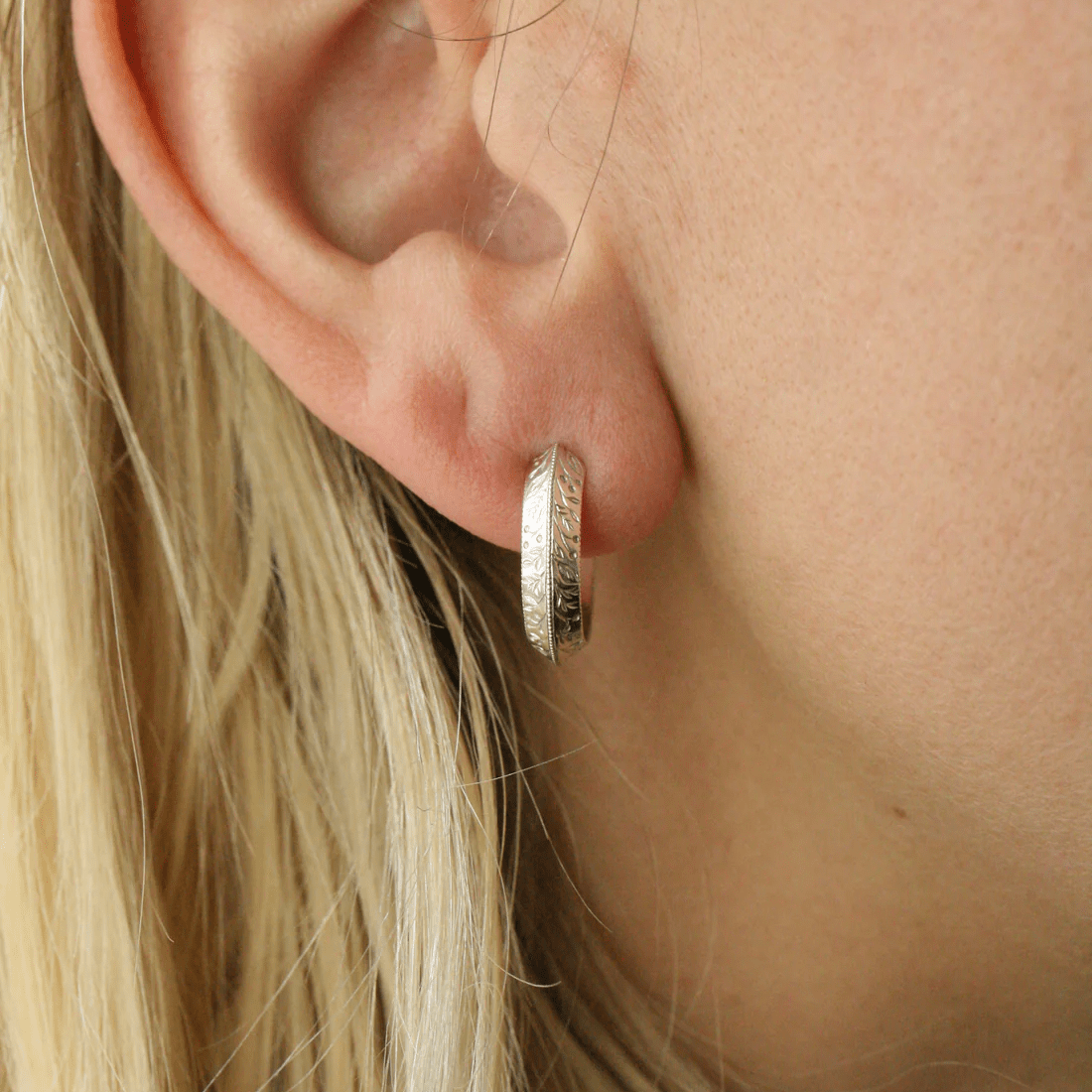 Side view of a 14k gold floral engraved hoop earring worn on the ear.