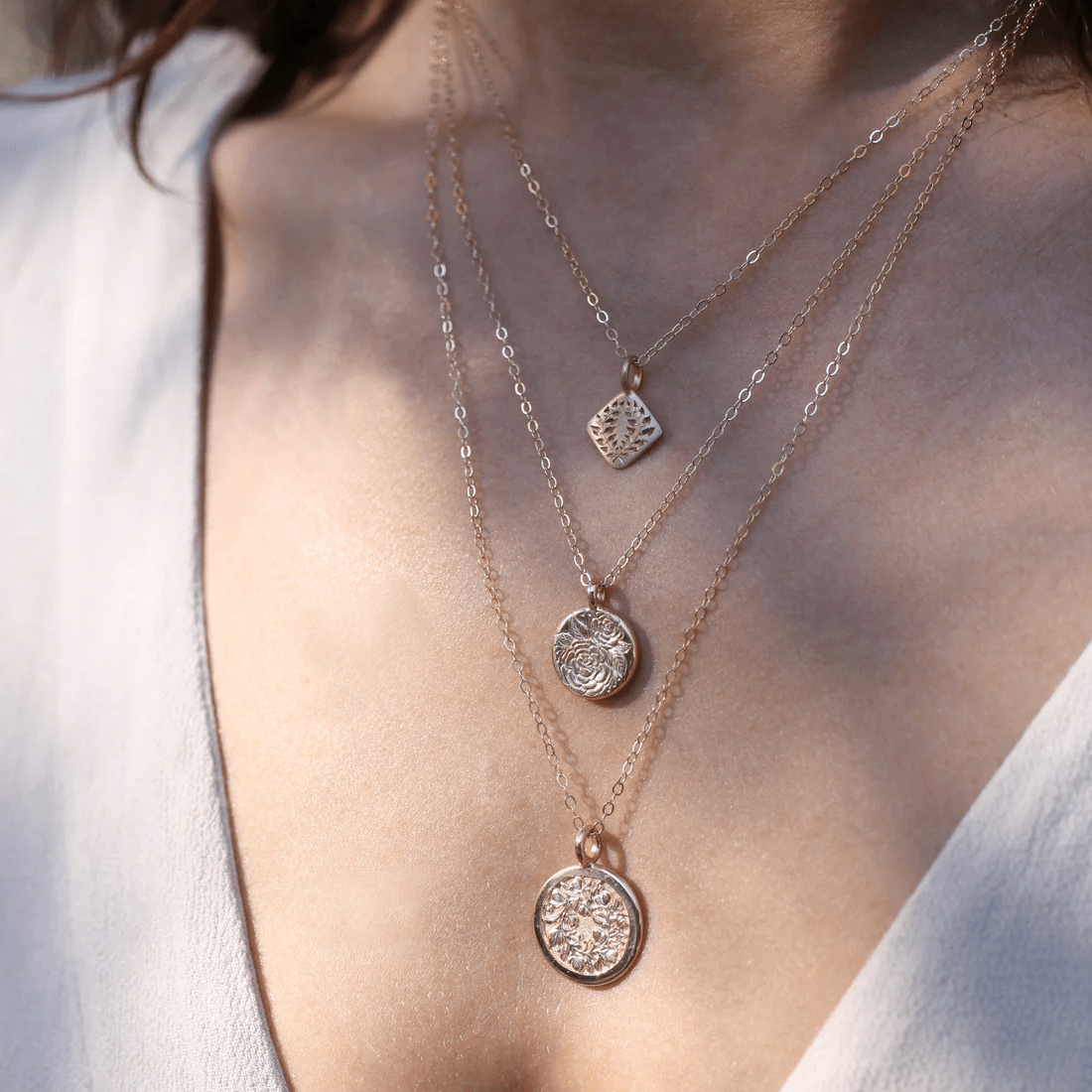Layered necklaces featuring a 14k gold laurel square pendant worn on the neck, shown on a model.