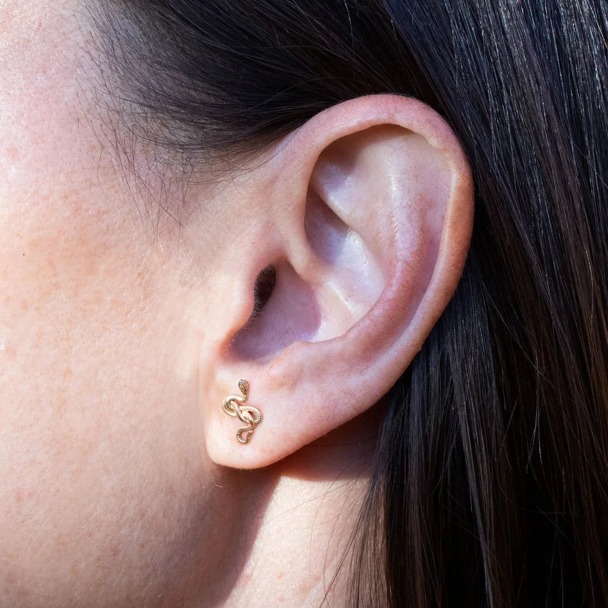 Close-up of a 14k yellow gold Snake Guardian Stud Earring worn on the ear, highlighting its miniature coiled snake design.