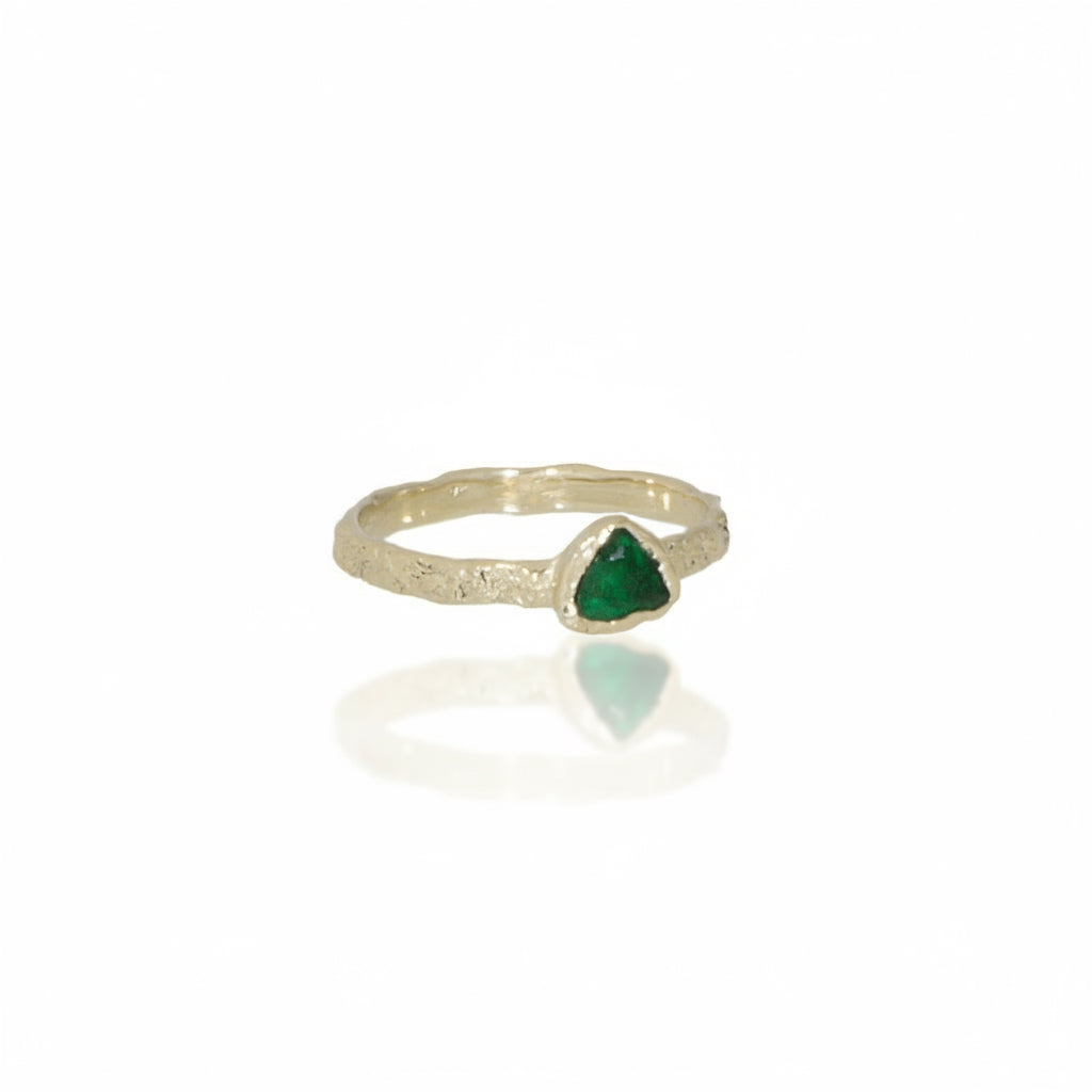 Angled view of the handcrafted 14k yellow gold Metamorphic Ring, showing its triangular green emerald, organic rock-inspired setting, and textured gold band.