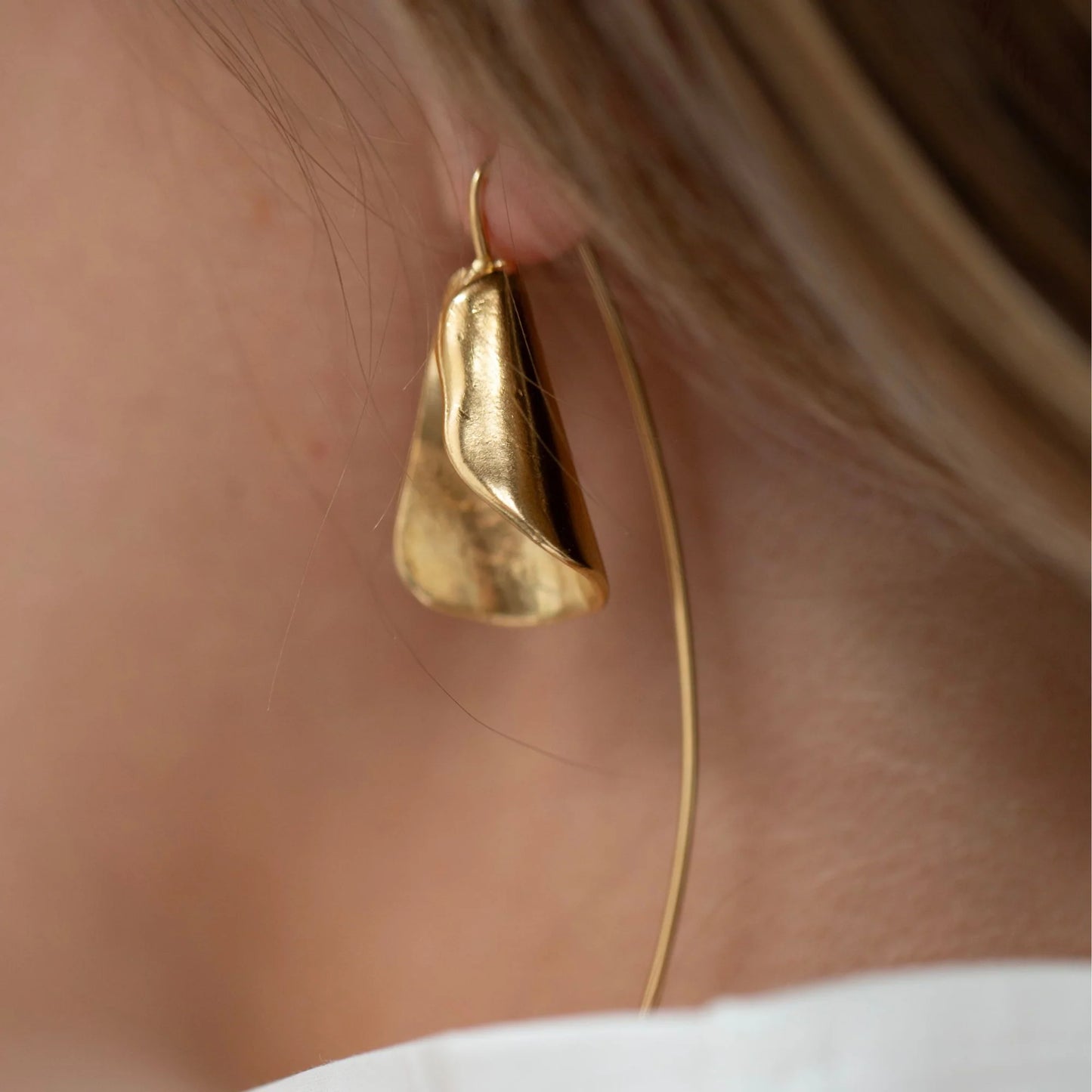 Gold hoop earring worn by a person with a neutral background
