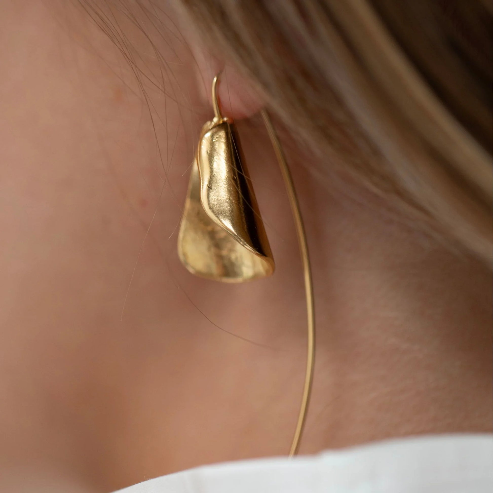Gold hoop earring worn by a person with a neutral background
