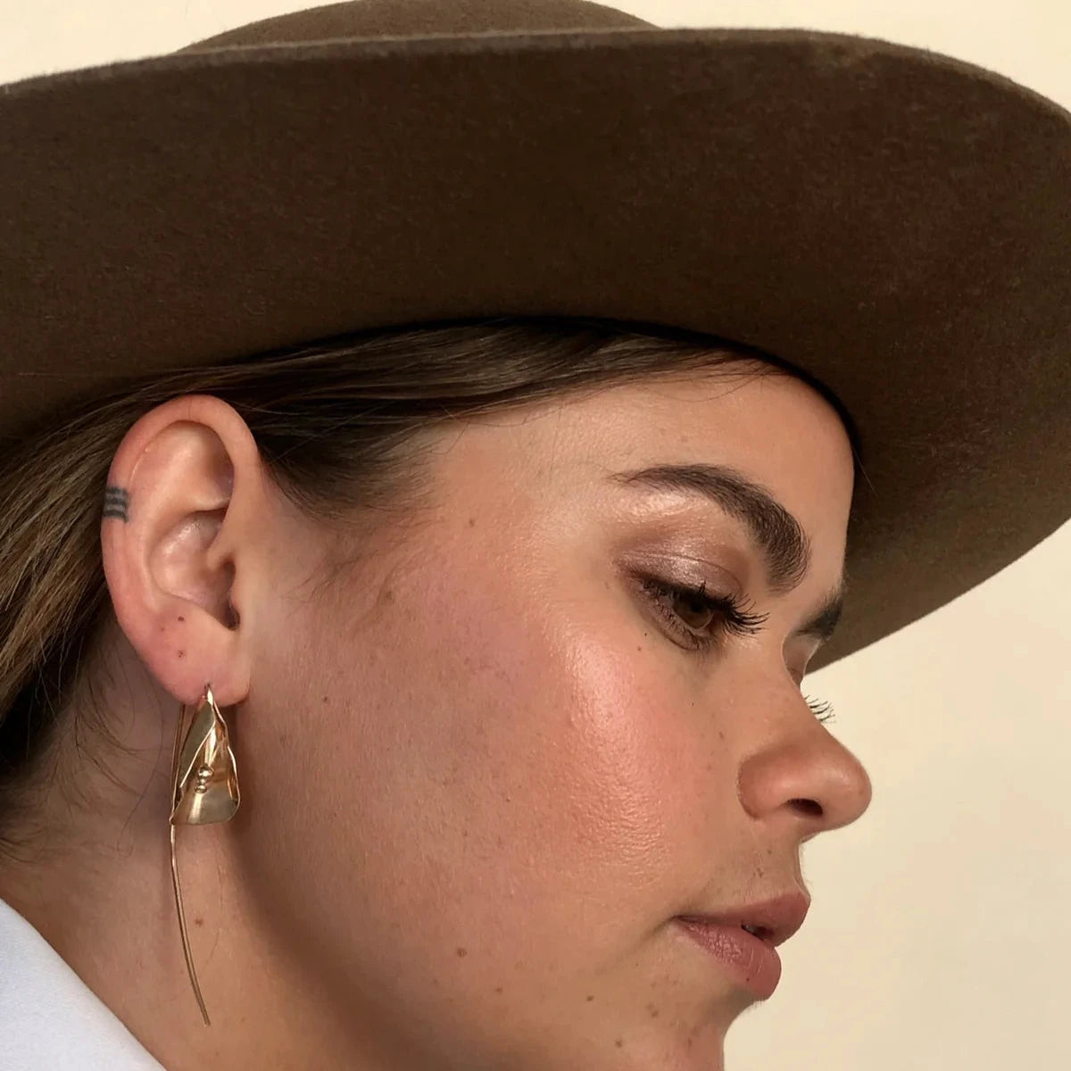 Person wearing a brown hat and gold earring on a beige background