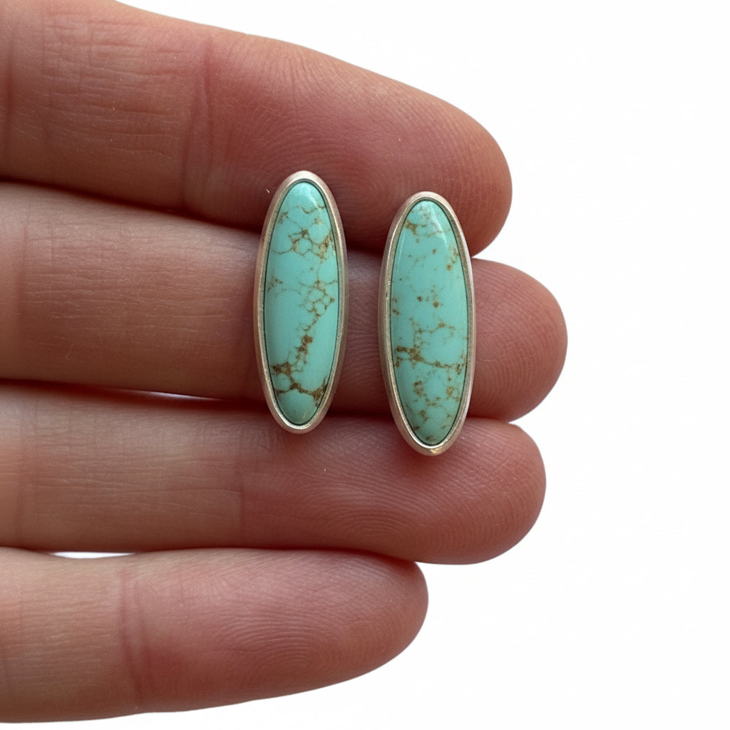 Turquoise stone earrings held between fingers on a white background