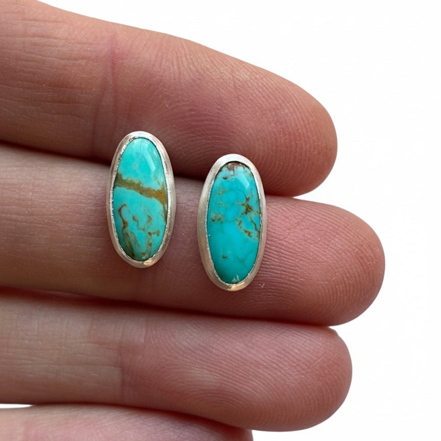 Turquoise stone earrings held between fingers on a white background