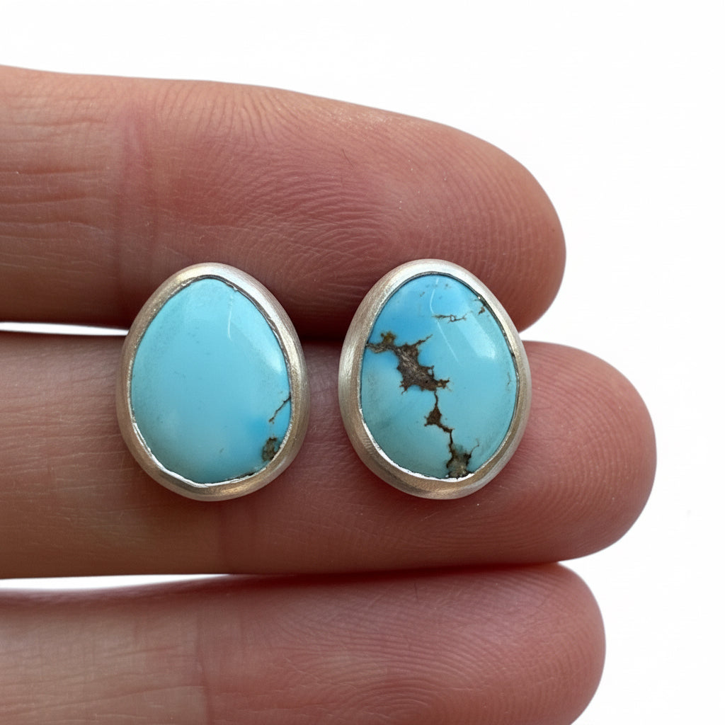Turquoise stone earrings held between fingers on a white background