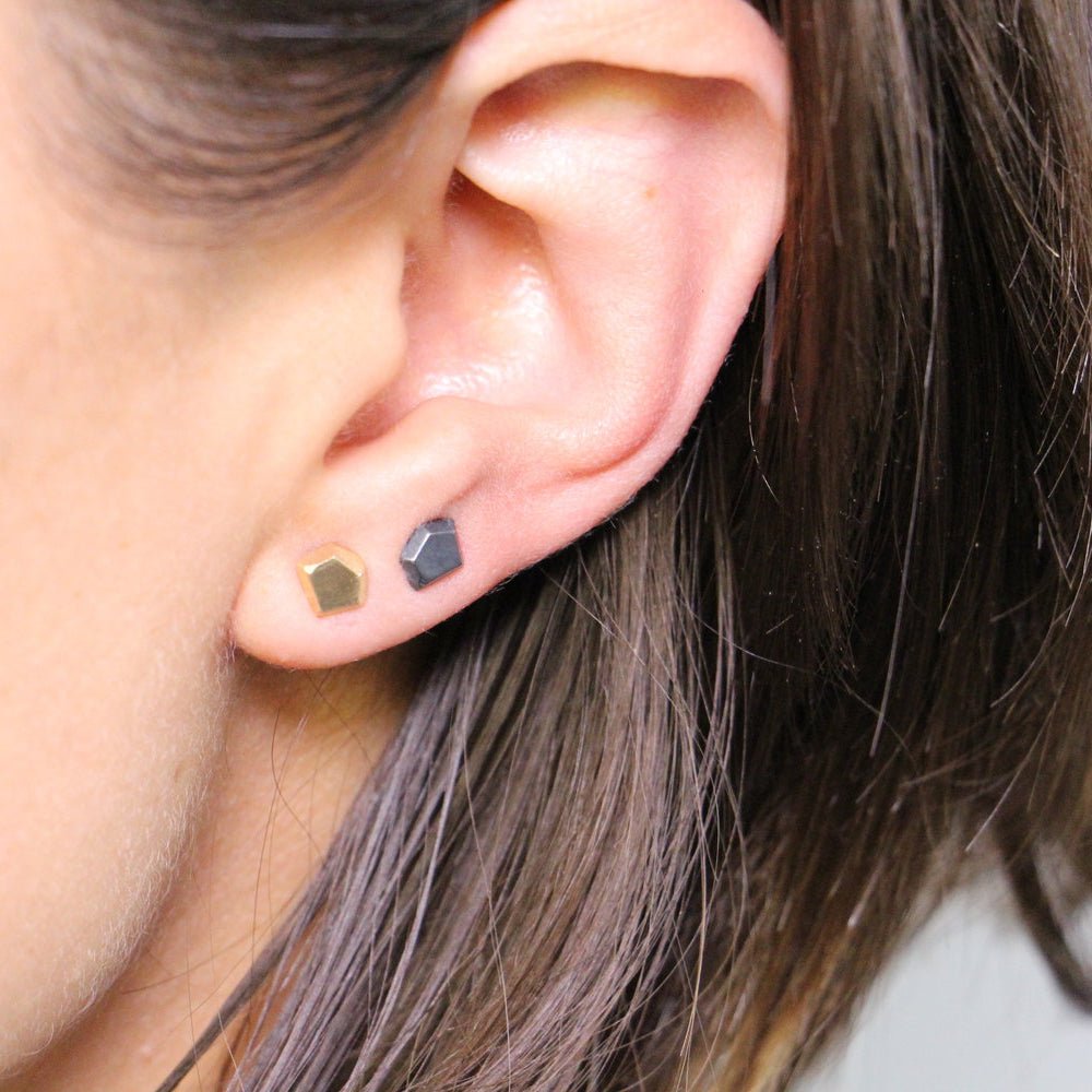 Close-up of a person wearing two earrings, one gold and one silver.