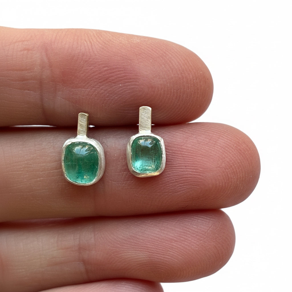 Green tourmaline earrings held between fingers on a white background