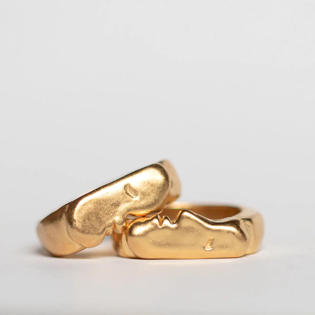 Two gold kiss signet rings on a light gray background