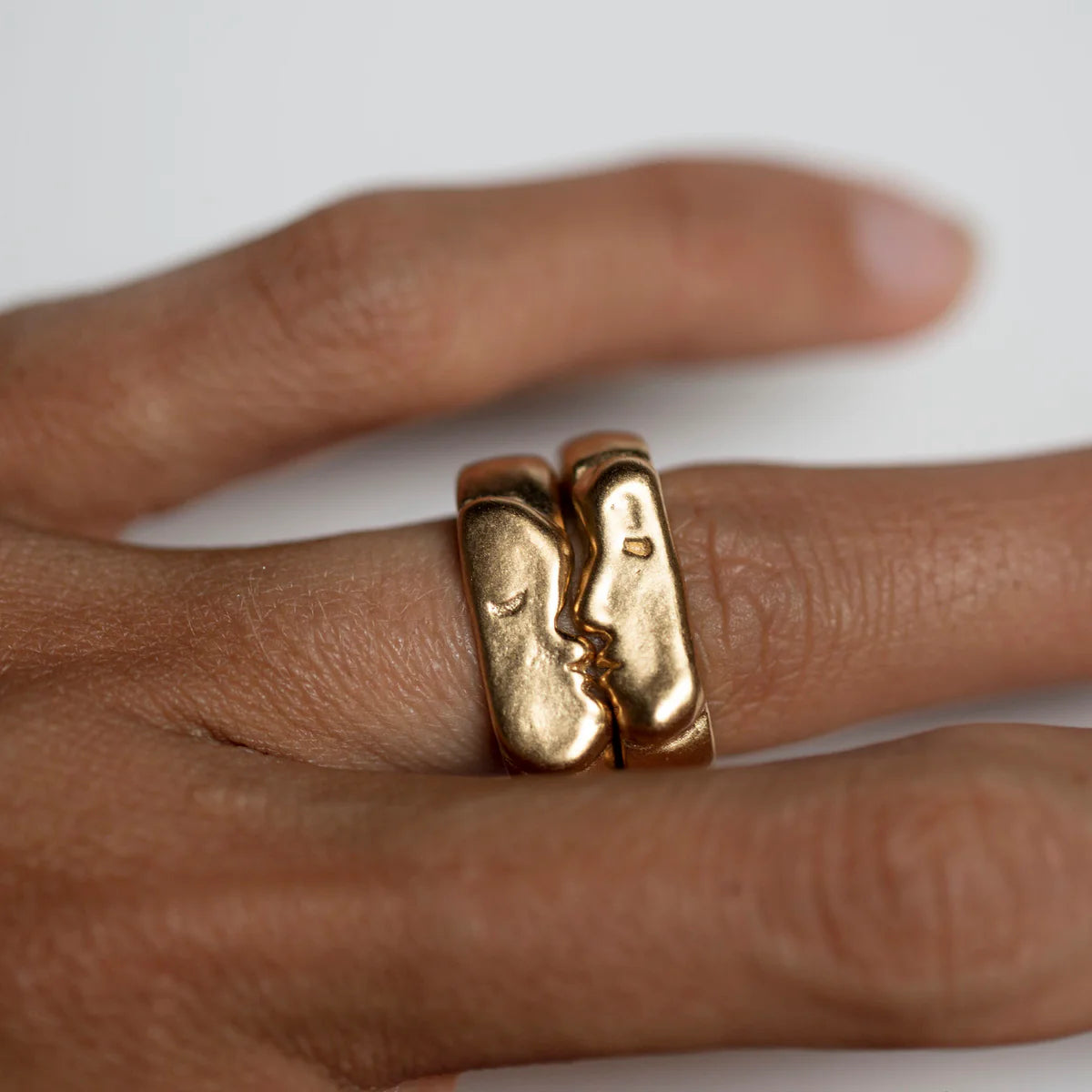 Gold rings with a unique kiss signet design on a finger against a neutral background