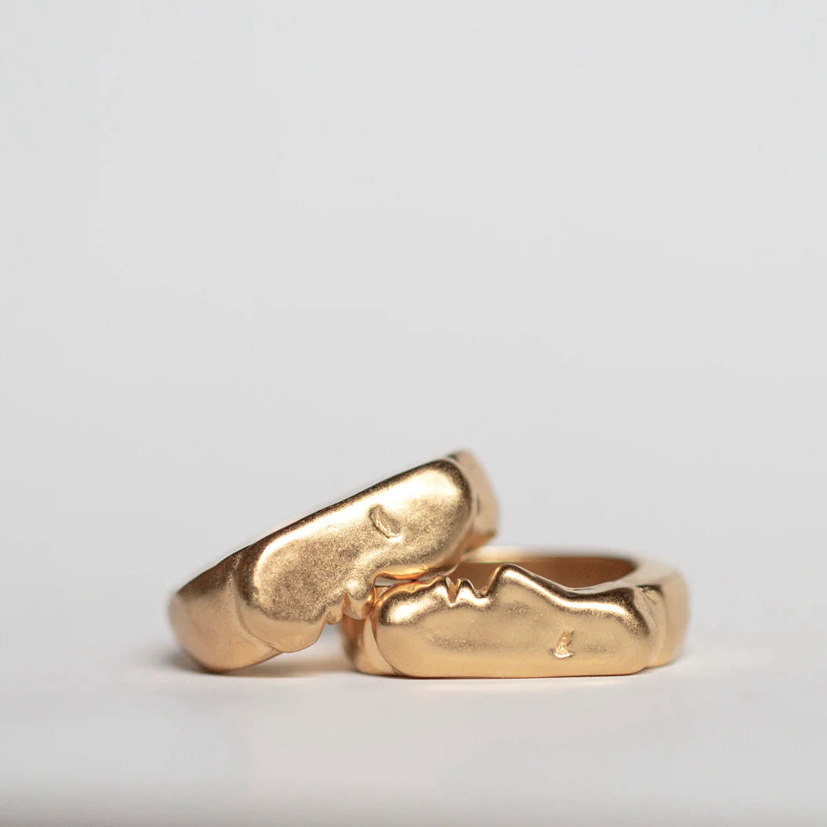Two gold kiss signet rings on a light gray background