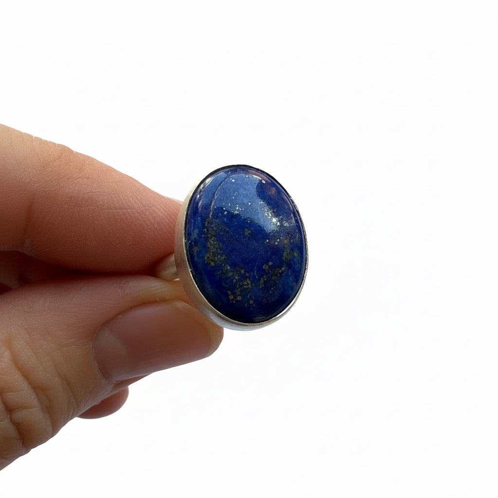 Ring with a lapis lazuli stone held by a hand against a white background