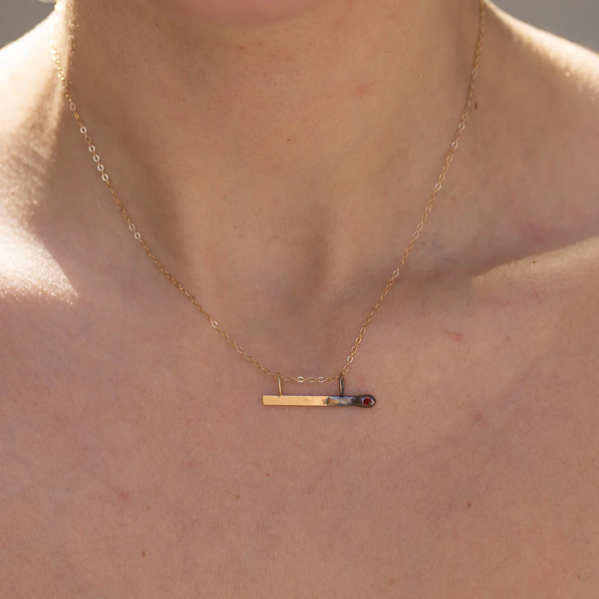 Necklace with a unique horizontal match charm on a person's neck.