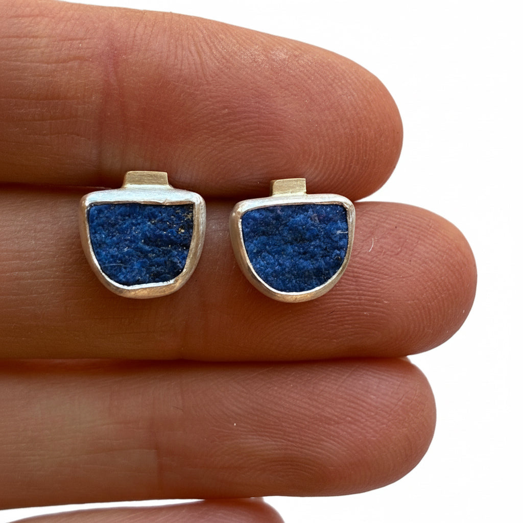 Gold and silver earrings with blue lapis stone on a finger against a neutral background