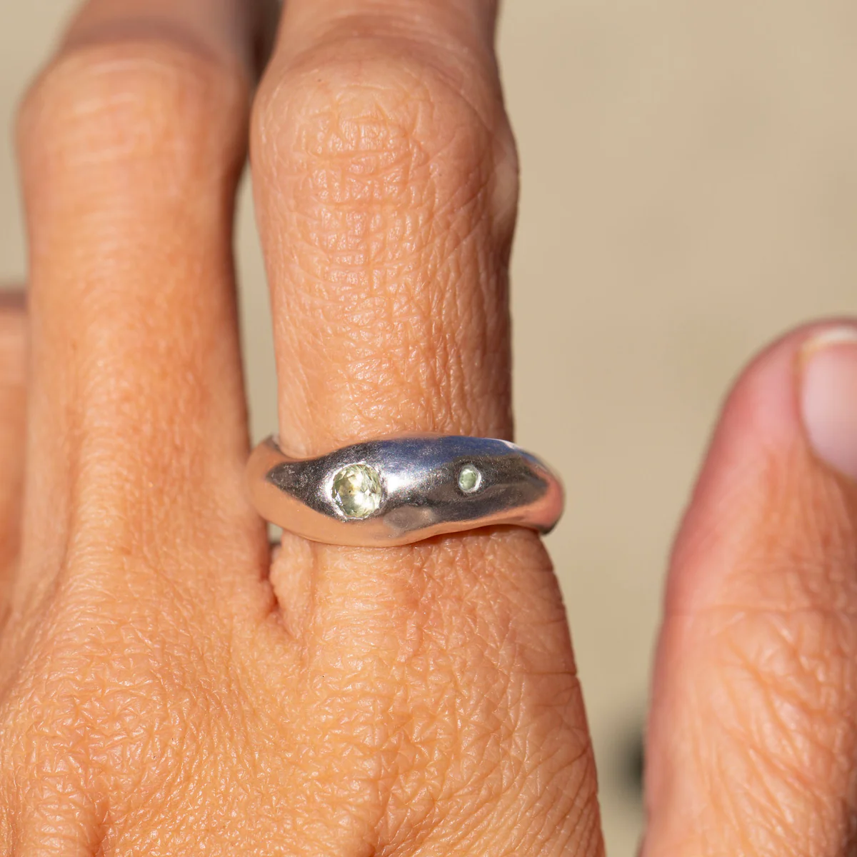 Silver ring with green gemstones on a finger against a neutral background