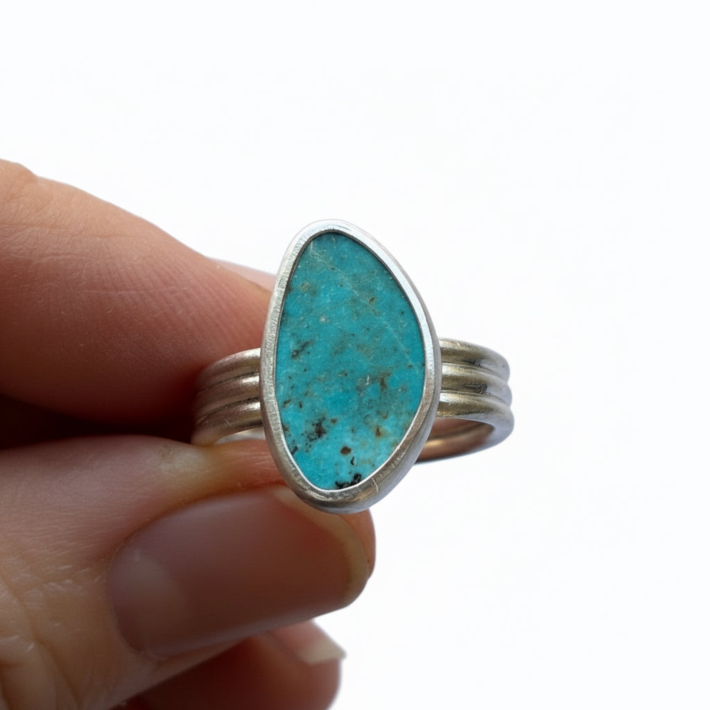 Turquoise ring with silver band held by a hand on a white background