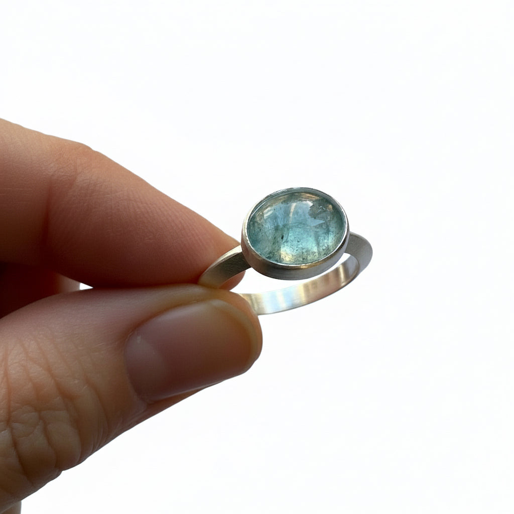 Silver ring with a tourmaline gemstone held in a hand against a white background