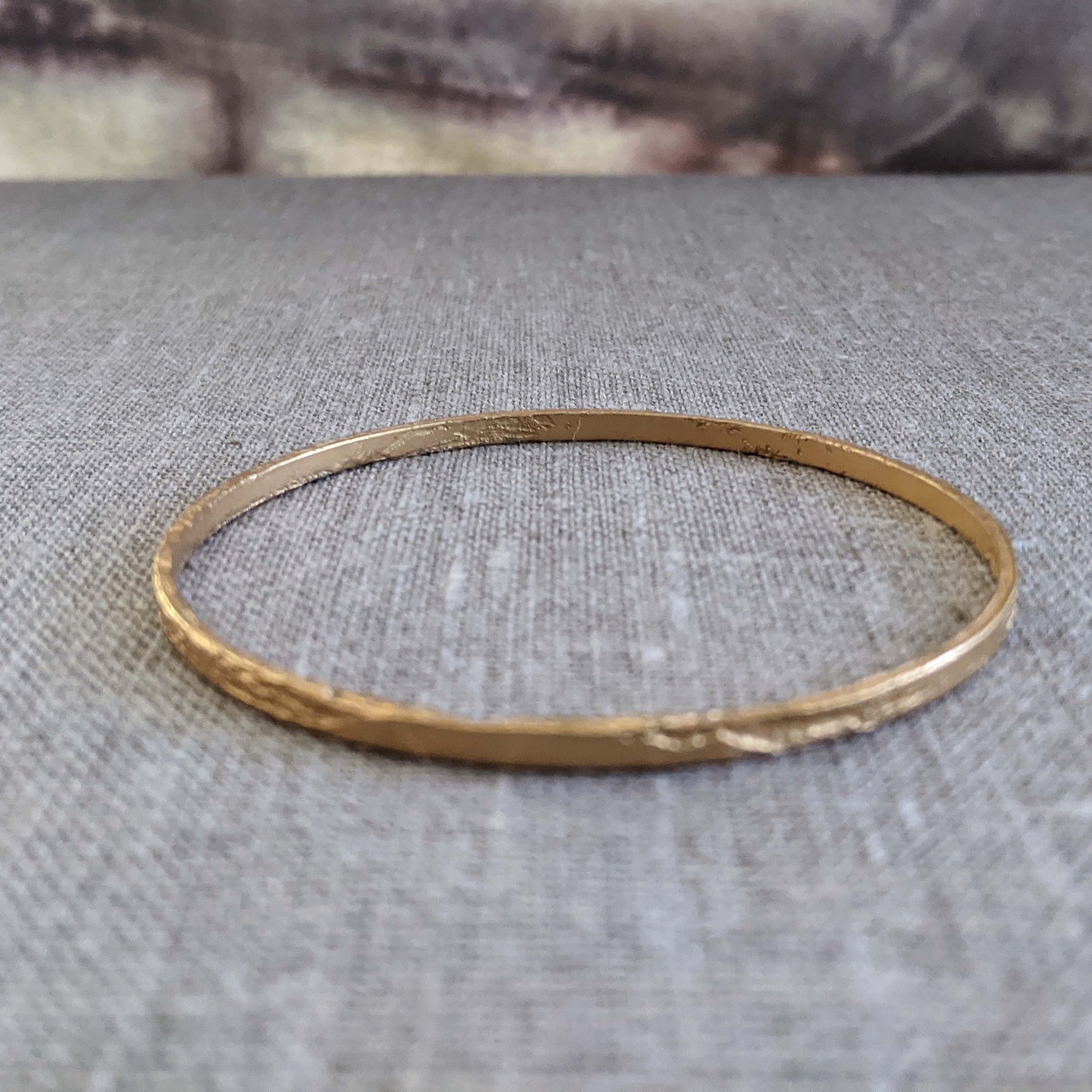 Single thin etched bangle in 22k gold-plated brass shown on a textured grey surface.