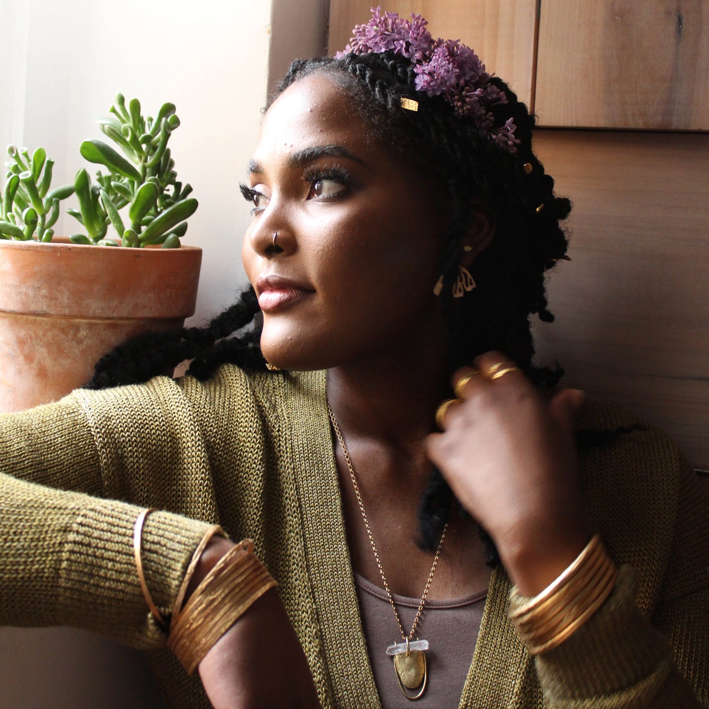 Model wearing multiple thin etched gold bangles in a natural indoor setting.