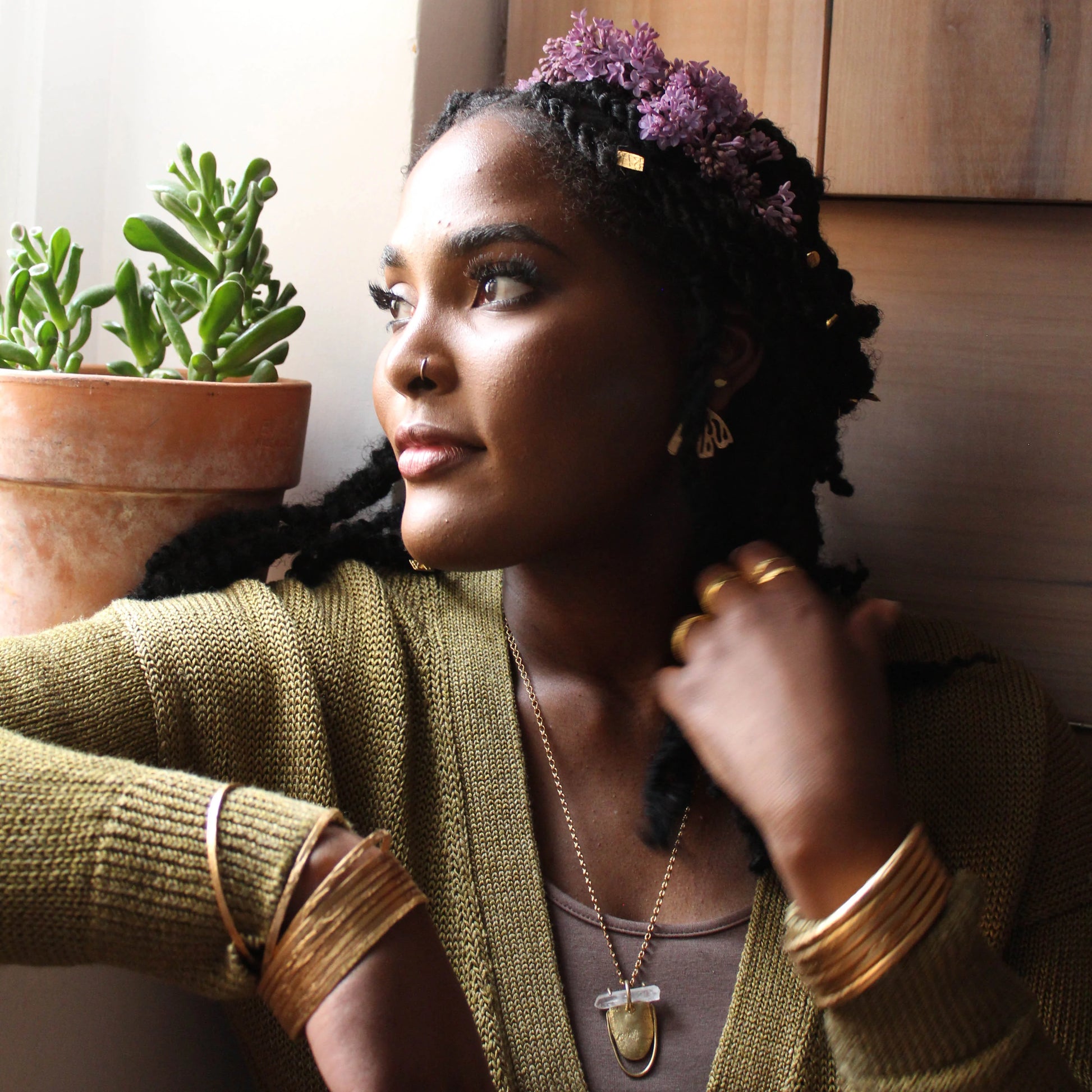 Model wearing multiple thin etched gold bangles in a natural indoor setting.