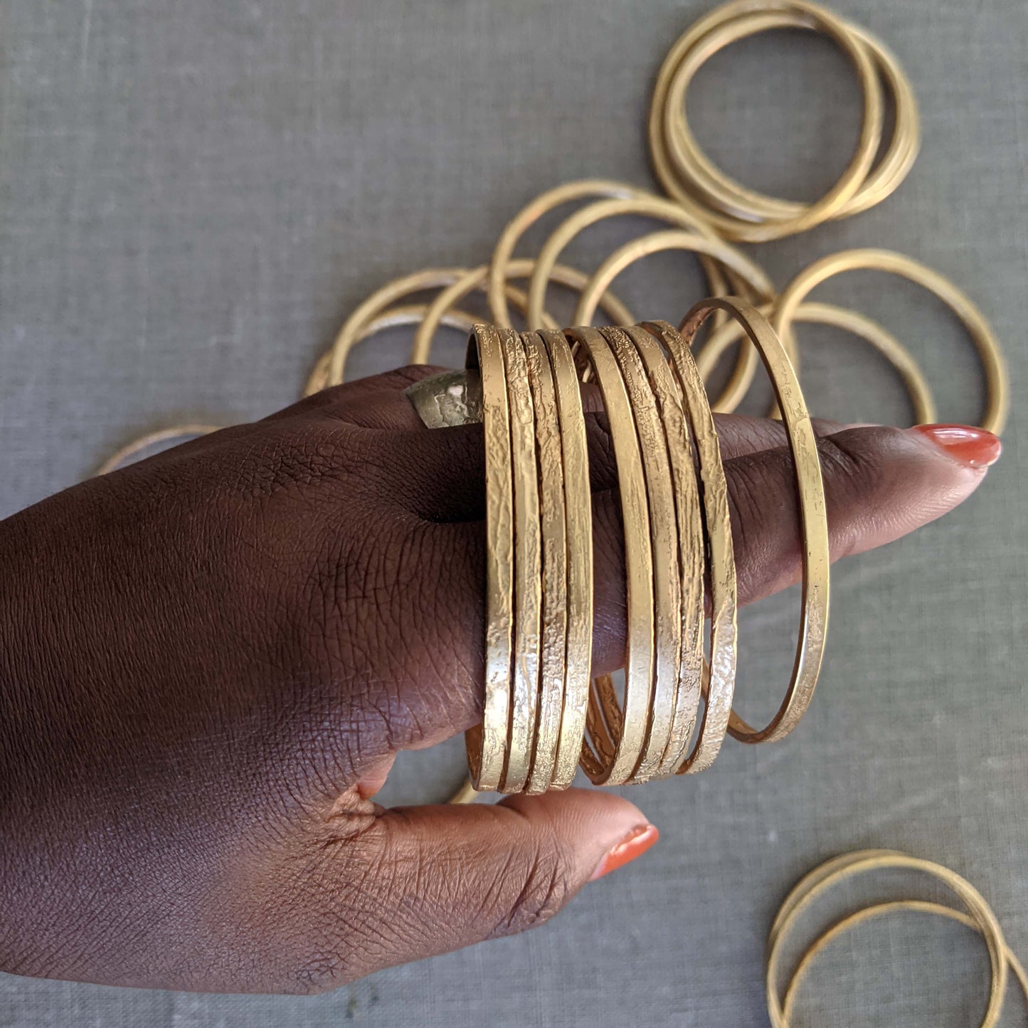 Hand wearing a large stack of thin etched gold bangles, showing texture and shine.
