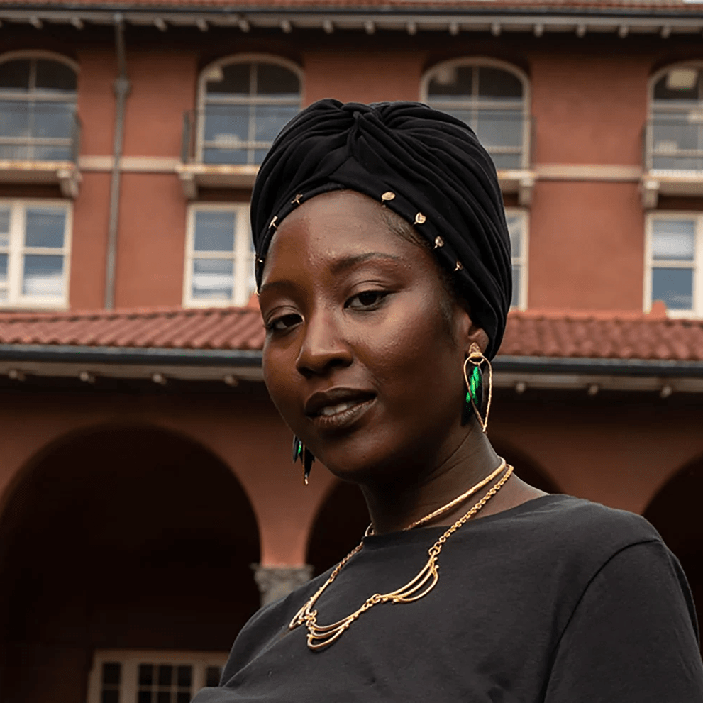 Model wearing iridescent beetle wing earrings outdoors, showing natural green tones and gold-plated brass design.