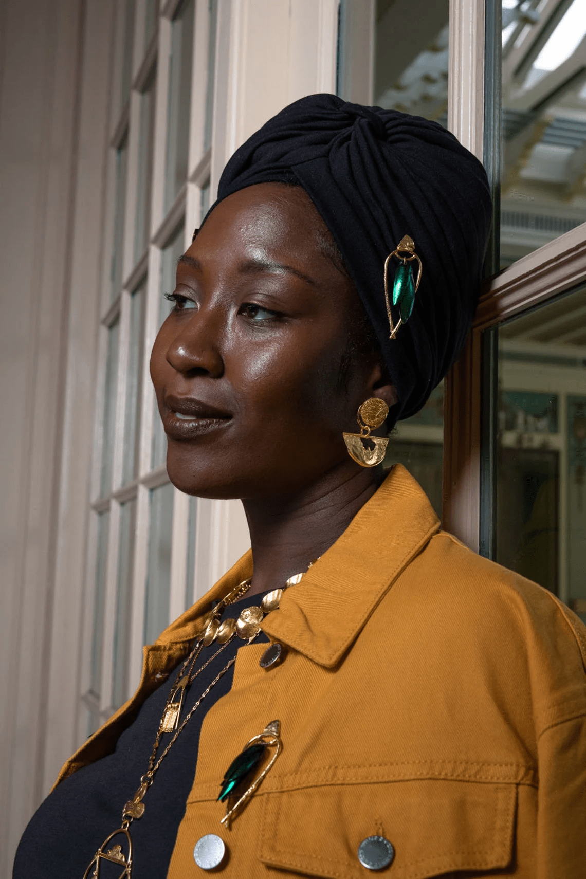 Side-profile portrait of model wearing green beetle wing earrings framed in gold-plated brass.